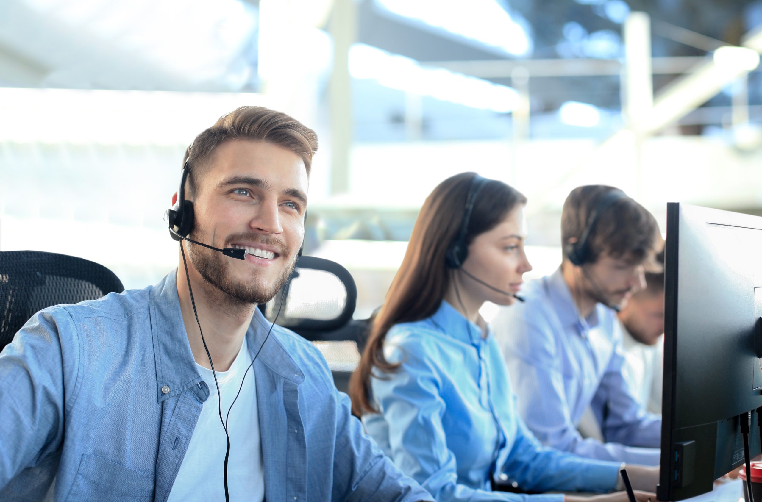 smiling-call-center-employees-sitting-line-with-their-headset-scaled